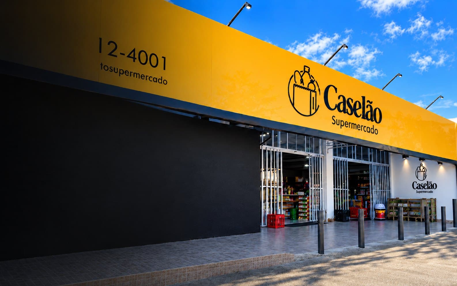 Fachada do supermercado com a placa amarela, a parede preta e a entrada de vidro sob o céu azul